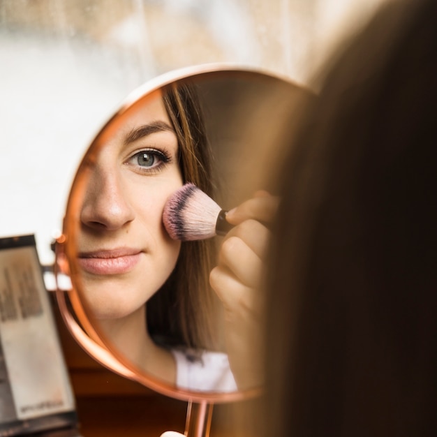 Hand mirror with reflection of woman applying blusher on her face Free Photo