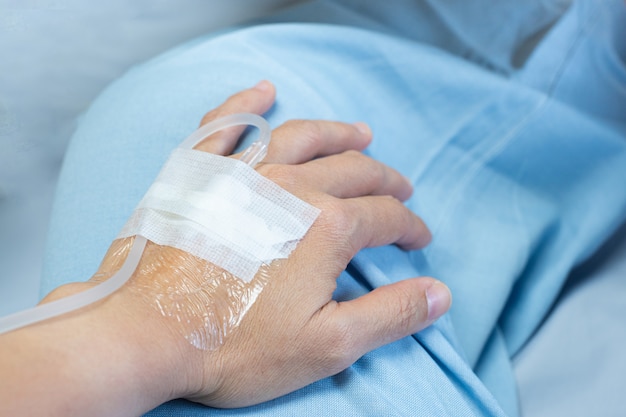 生理食塩水チューブ注射と手に滅菌石膏包帯を病院の病棟のベッドに横になっている患者の手 プレミアム写真