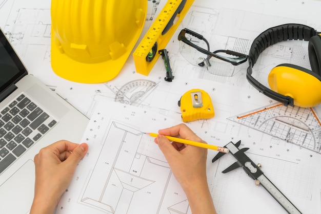 Hand over Construction plans with yellow helmet and drawing tool Free Photo