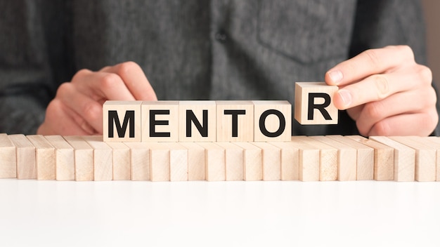 Premium | The hand puts a wooden cube with r from the word mentor