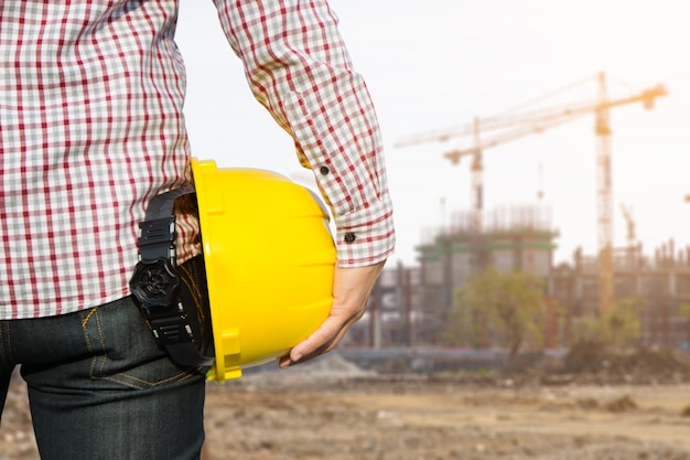 Hand's engineer worker holding yellow safety helmet with building on site background. Free Photo Hand's engineer worker holding yellow safety helmet with building on site background. Free Photo