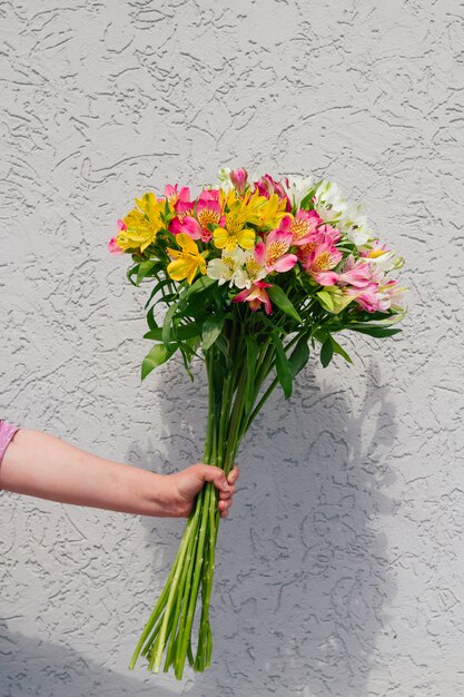 粗いコンクリートの壁にアルストロメリアの花の花束を持つ手 プレミアム写真