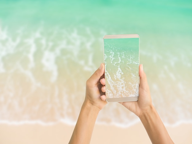ビーチの海の波 休日の夏のぼかし画像にモバイルビュー青い海砂ビーチを保持している手の女性 プレミアム写真