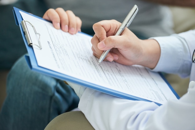 Hands of unrecognizable female doctor filling in form on clipboard Free Photo