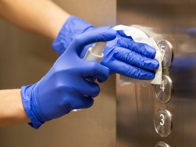 Hands with surgical gloves disinfecting elevator buttons Free Photo