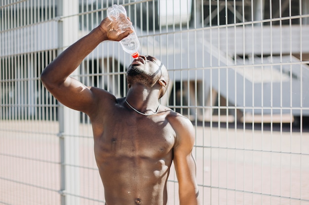 裸の胸のポーズで水のボトルでハンサムなアフリカ系アメリカ人の男 無料の写真