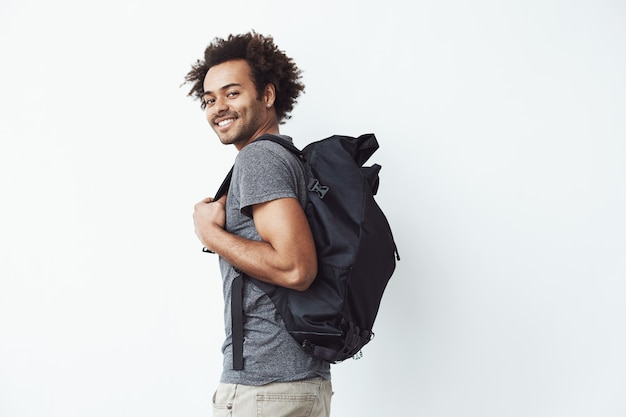 Handsome african man with backpack smiling standing against white wall ready to go hiking or a student on his way to university. Free Photo