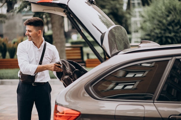 Handsome business man standing by his car on a business trip | Free Photo