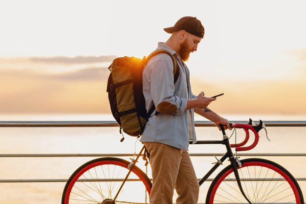 海沿いの朝の日の出にバックパックと自転車で旅行する電話を使用して 