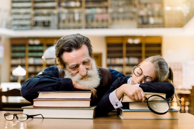 Premium Photo Handsome Man Grandfather And Pretty Little Girl Granddaughter Fell Asleep During Reading Books In Old Ancient Library Sitting At The Table Over The Vintage Book Shelves Background