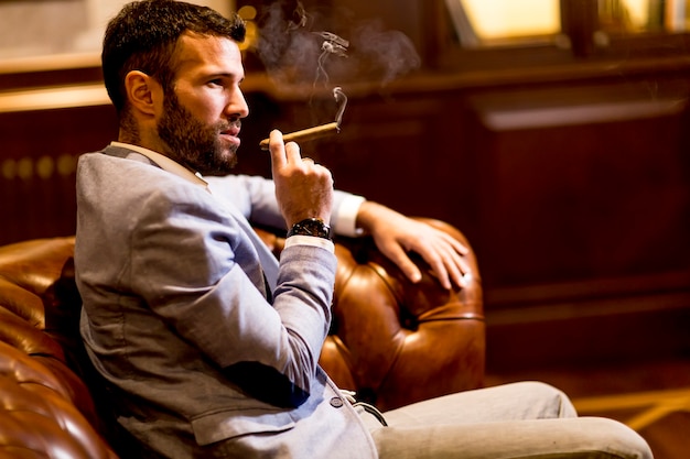 Premium Photo | Handsome man sitting on a leather sofa and smoking cigar