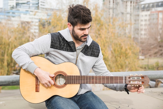 Handsome young man sitting in the park playing guitar