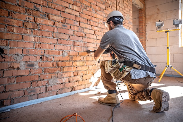 Handyman at a construction site in the process of drilling a wall with a perforator Free Photo