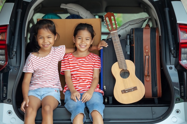 ギターを弾き 車のトランクで彼女の妹と歌を歌う幸せなアジアの子供の女の子 プレミアム写真