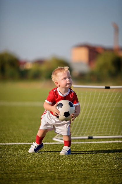 ゲート近くのフィールドでボールとサッカーをして幸せな赤ちゃん男の子 プレミアム写真