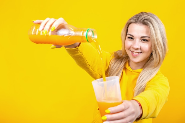 ペットボトルからグラスにオレンジジュースを注ぐカジュアルなスポーティな服で幸せな美しい若いブロンドの女性 プレミアム写真