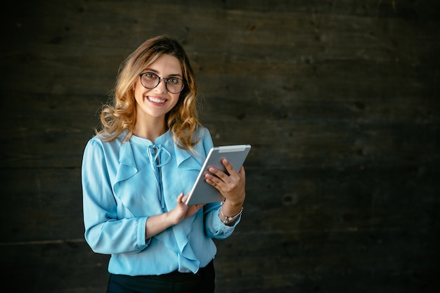 Happy beautiful young business woman standing with tablet, widely smiling. Free Photo