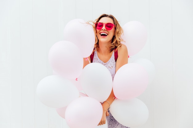 Happy beautiful young woman in pink sunglasses holds white balloons, cheerfully smiling Free Photo