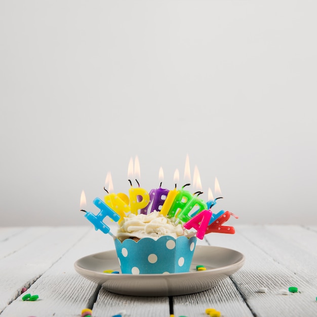 白い背景に対してセラミックプレート上のカップケーキの上の誕生日おめでとう手紙キャンドル 無料の写真