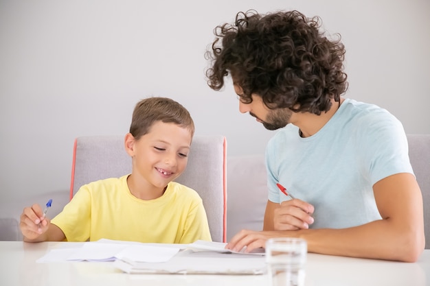幸せな少年と彼のお父さんは一緒に学校の家の仕事をし 論文を書き レッスンについて話し合っています 家族とゲイの両親の概念 無料の写真