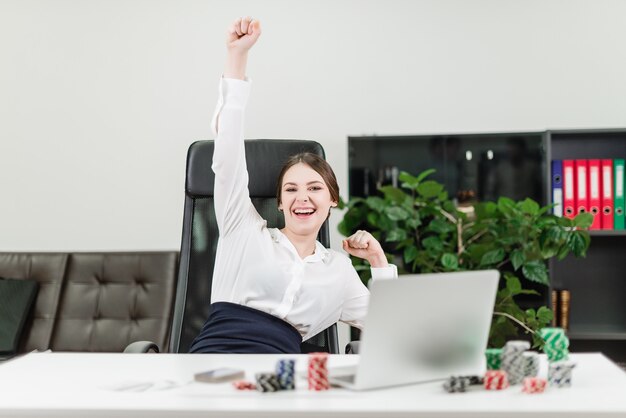 Happy businesswoman wins in online casino while playing poker in the office at workplace Premium Photo