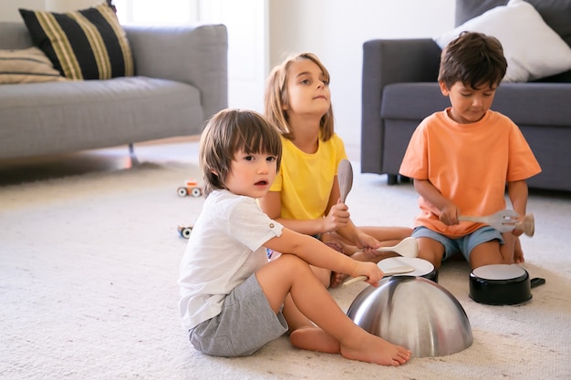 じゅうたんの上に座って道具で遊んでいる幸せな子供たち かわいい白人の男の子とブロンドの女の子が居間で一緒に楽しんで 鍋をノックします 子供の頃と家庭の活動の概念 無料の写真