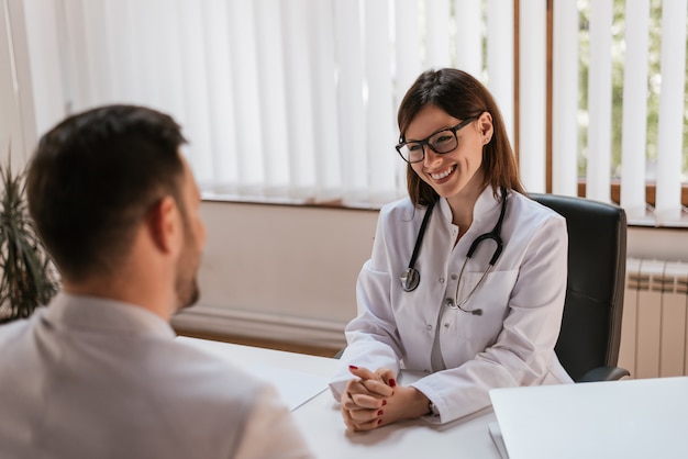 Happy female doctor discussing with patient at table in clinic Premium Photo