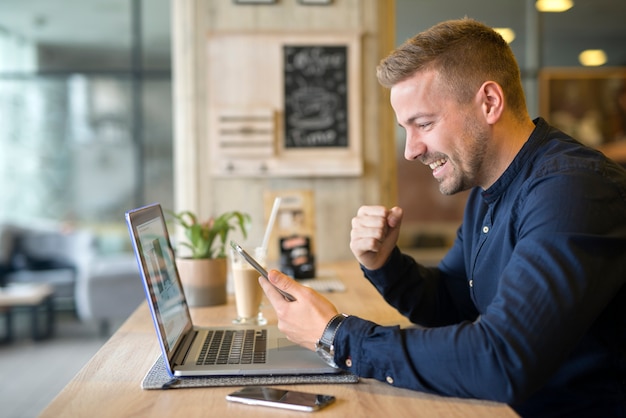 Happy freelancer with tablet and laptop computer in coffee shop Free Photo