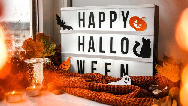 Premium Photo Happy Halloween Text In White Light Box With A Background Of Sweater Dried Leaves Halloween Autumn Decoration On The Windowsill Rainy Window Bokeh Light Ghost Pumpkins Bat Black Cat