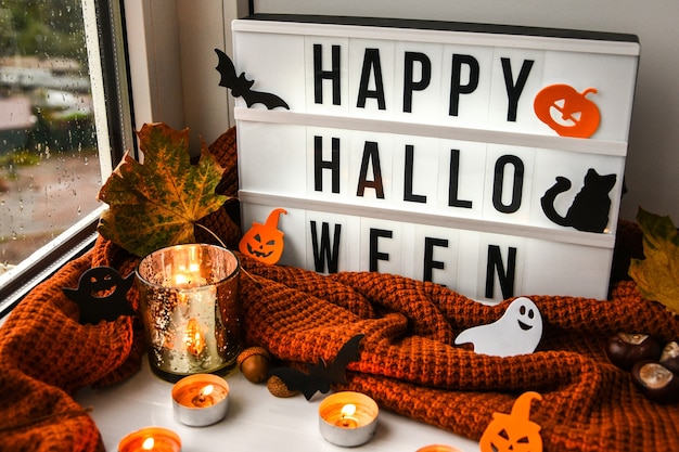 Premium Photo Happy Halloween Text In White Light Box With A Background Of Sweater Dried Leaves Halloween Autumn Decoration On The Windowsill Rainy Window Bokeh Light Ghost Pumpkins Bat Black Cat