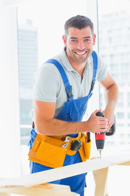 Premium Photo | Happy handyman drilling plank in office