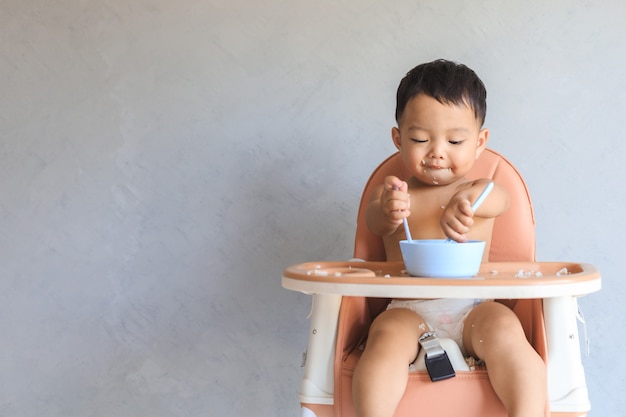 赤ちゃんのハイチェアに座って コピースペースで一人で食べ物を食べる幸せな幼児アジアの男の子 プレミアム写真