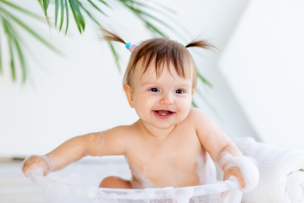 幸せな小さな女の赤ちゃんは洗面器で洗って遊ぶ プレミアム写真