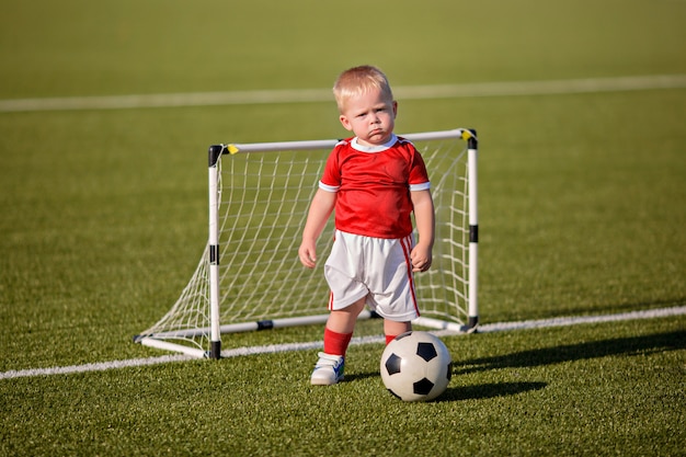 Premium Photo | Happy little boy in sports uniform playing soccer with
