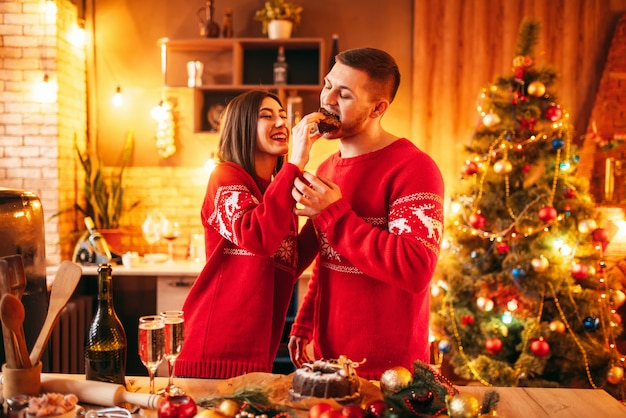 幸せな愛のカップル 妻は夫にクリスマスケーキ お祝いの食べ物を供給しています 一緒にクリスマスのお祝い 若い家族の幸せ プレミアム写真