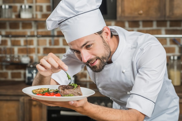 Happy male chef preparing beef steak with vegetable decoration ...