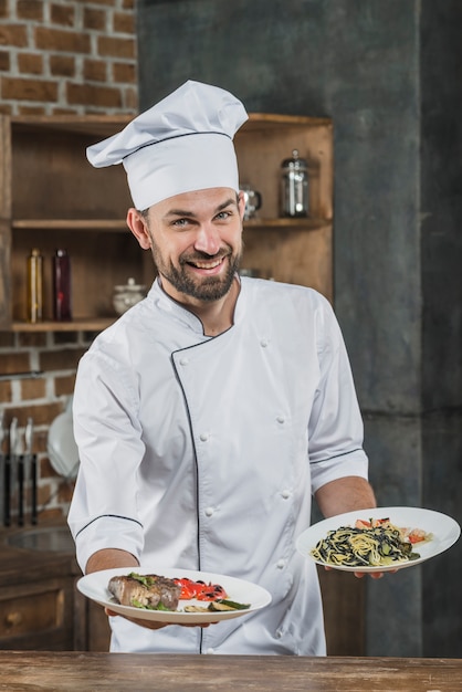 Happy male chef in white uniform offering delicious dishes | Free Photo