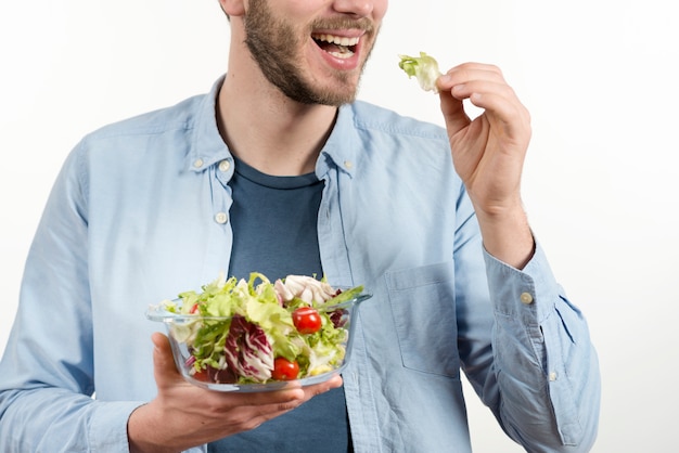 Happy man eating healthy salad against white backdrop | Free Photo