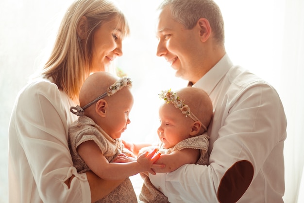Happy mom and dad pose with funny twins on their arms before a bright window  Free Photo