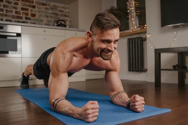 Premium Photo | A happy muscular man with a naked torso is doing a plank on  a blue yoga mat in his apartment in the evening