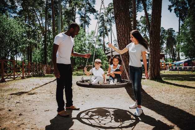 Premium Photo Happy Parents Pushing Kids On Swing On Playground