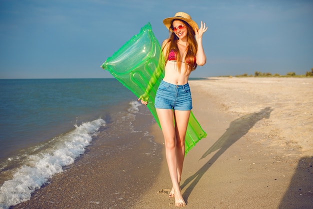 Free Photo Happy Pretty Woman Having Fun On Beach Wearing Stylish Beachwear Bikini Hat And Denim Shorts Long Legs Slim Fit Body Holding Air Mattress And Walking Near Ocean