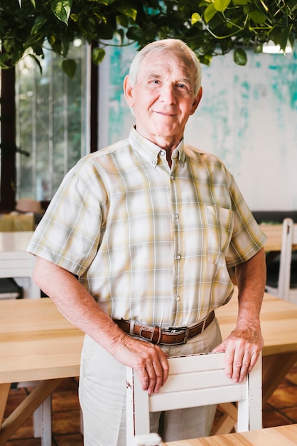 Happy Senior Male Standing In Cafe Leaning On Chair Photo Free