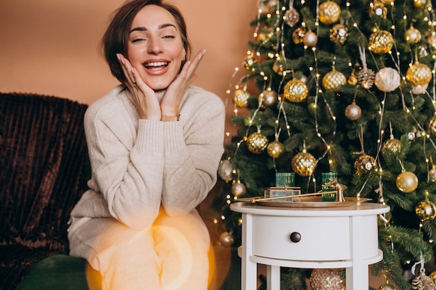 Happy woman sitting on sofa by the christmas tree Free Photo