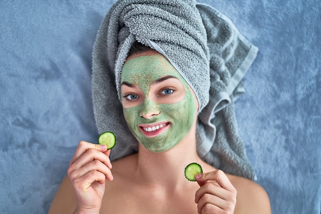 Premium Photo | Happy woman with green cleansing clay mask and cucumber  slices in bath towel is resting and relaxing during spa day at home. face  skin care