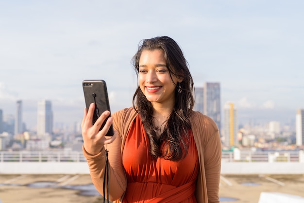 Premium Photo | Happy young beautiful indian woman using phone against view  of the city