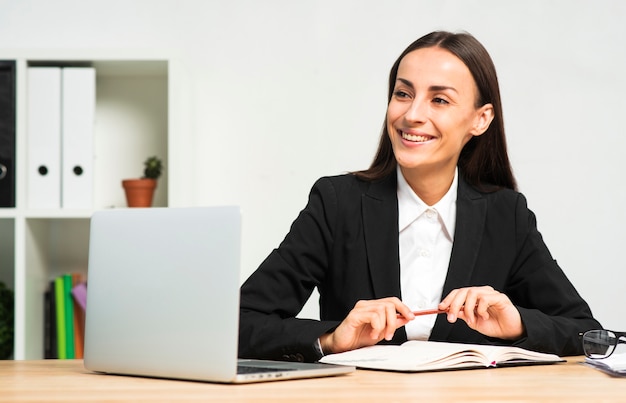 Happy Young Businesswoman Sitting Behind The Desk With Book Pen