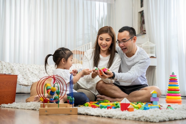Happy young father and mother and a little daughter playing with toy wooden blocks, sitting on the floor in living room, family, parenthood and people concept with developmental toys Premium Photo
