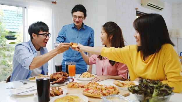 Happy young friends group having lunch at home. asia family party eating pizza food and laughing enjoying meal while sitting at dining table together at house. celebration holiday and togetherness. Free Photo