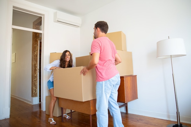 Happy young hispanic couple moving into new flat, carrying carton boxes and furniture Free Photo